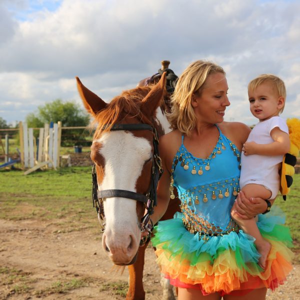 sorrel and white paint mare hangs her head quietly while equine trainer MacCoy gets silly with little baby dressed in halloween bumble bee outfit