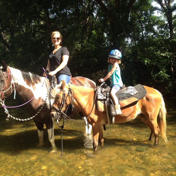 Smiling little girl on cute flaxen mane pony standing in the water with mother, mounted on gorgeous black and white paint mare for sale in San Marcos, Texas