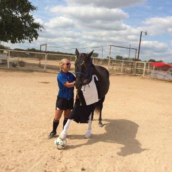 Texas horse trainer, MacCoy, stands with beloved mare, Black, who has her hoof planted firmly on a soccer ball after some summertime fun in Austin horseback riding stables